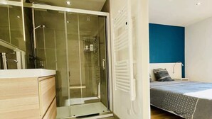 Ein modernes Schlafzimmer mit Glasdusche, einem Holzkleiderschrank, einem Bett mit gemustertem Überwurf und einer blauen Akzentwand.