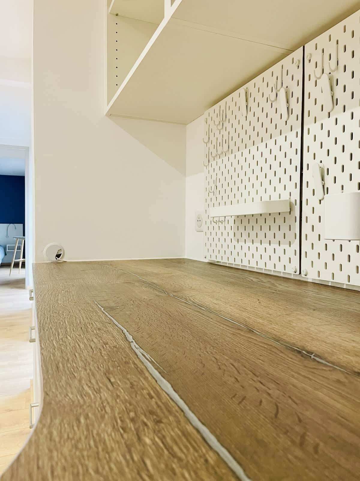 Une pièce avec un plancher en bois, un mur blanc orné d’un panneau perforé et une étagère blanche.