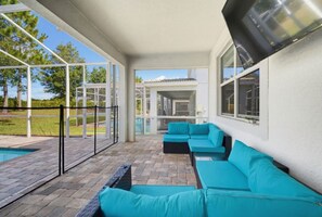 A covered outdoor seating area with a pool, a view of a house, and a clear sky.