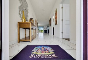 A hallway with a wooden console table, a purple doormat with the Storybook Vacation Homes logo, and a white door at the end.