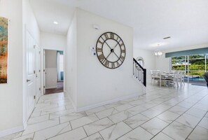 A spacious indoor area with a large wall clock, a staircase, and a dining area with outdoor views.