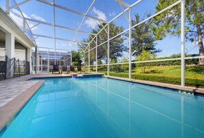 A clear blue swimming pool with a covered area, surrounded by a white fence and trees.