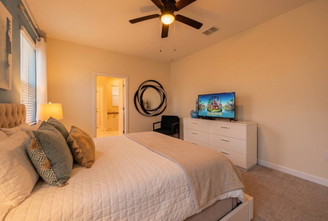 A bedroom with a bed, a ceiling fan, a TV, and a dresser.