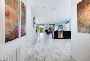 A modern kitchen with a central island, white tiled flooring, and artwork on the walls.