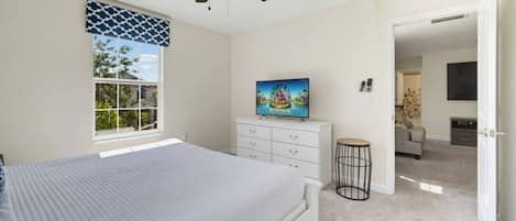 A bedroom with a bed, a ceiling fan, a dresser, a television, and a window with a view.