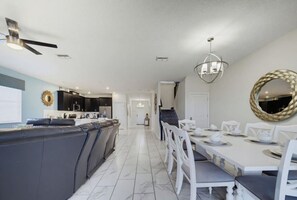 A modern kitchen with a central island, white dining table, and a staircase leading to an upper level. - Outstanding 8BR Resort Pool Home Near Disney World (Four Corners)