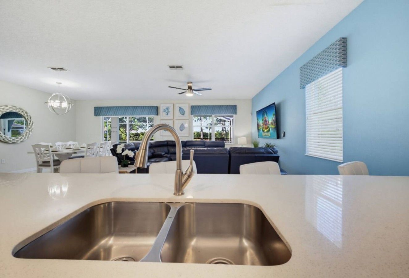 A modern kitchen with a stainless steel sink, a ceiling fan, and a dining area with a white table and chairs.