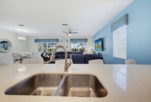 A modern kitchen with a stainless steel sink, a ceiling fan, and a dining area with a white table and chairs.