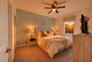 A bedroom with a bed, bedside tables, a ceiling fan, a window, and a television on a wooden cabinet.