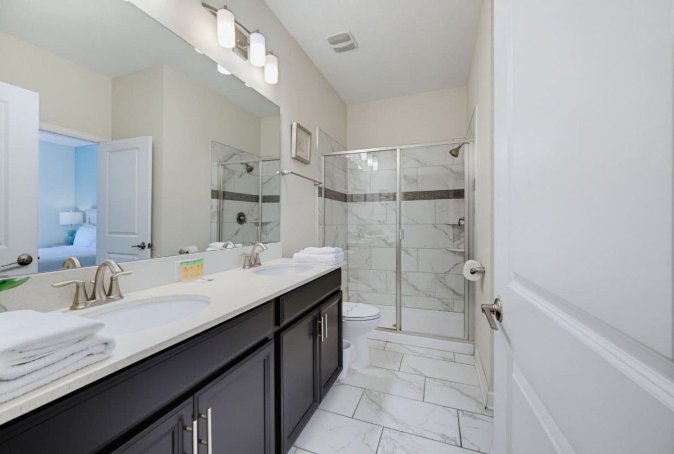 A modern bathroom with a double sink vanity, a glass shower enclosure, and a large mirror.