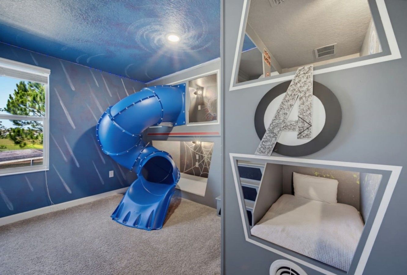 Una habitación con un tobogán azul, una cama con cabecera y una pared con diseño circular.