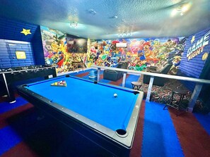 Een biljarttafel met een blauwe viltlaag, omringd door een levendige muurschildering met verschillende personages.