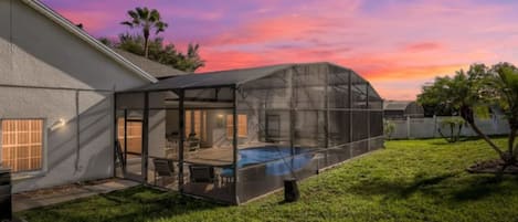 A house with a covered patio area, a swimming pool, and a lawn.