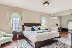 Een slaapkamer met een groot bed, een nachtkastje, een stoel en een raam met gordijnen.