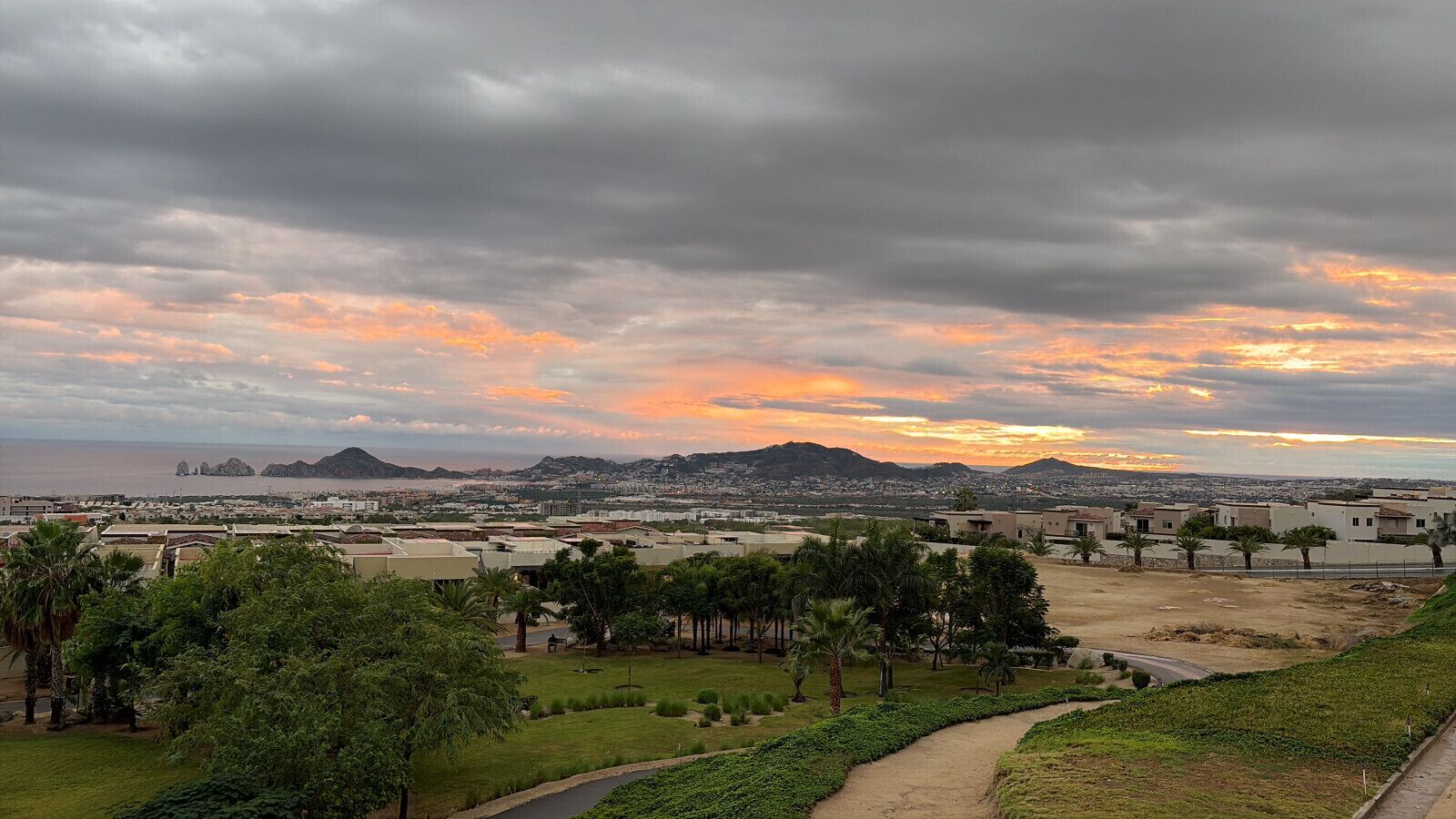 A cityscape with a view of a mountain range and the ocean during sunset.