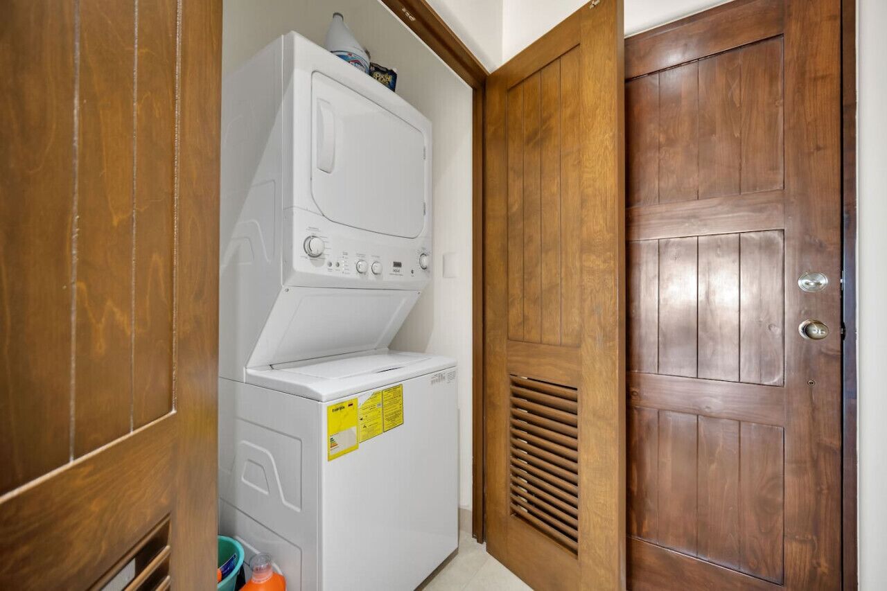 A laundry room with stacked washing machines and dryers, a wooden door, and a vent.