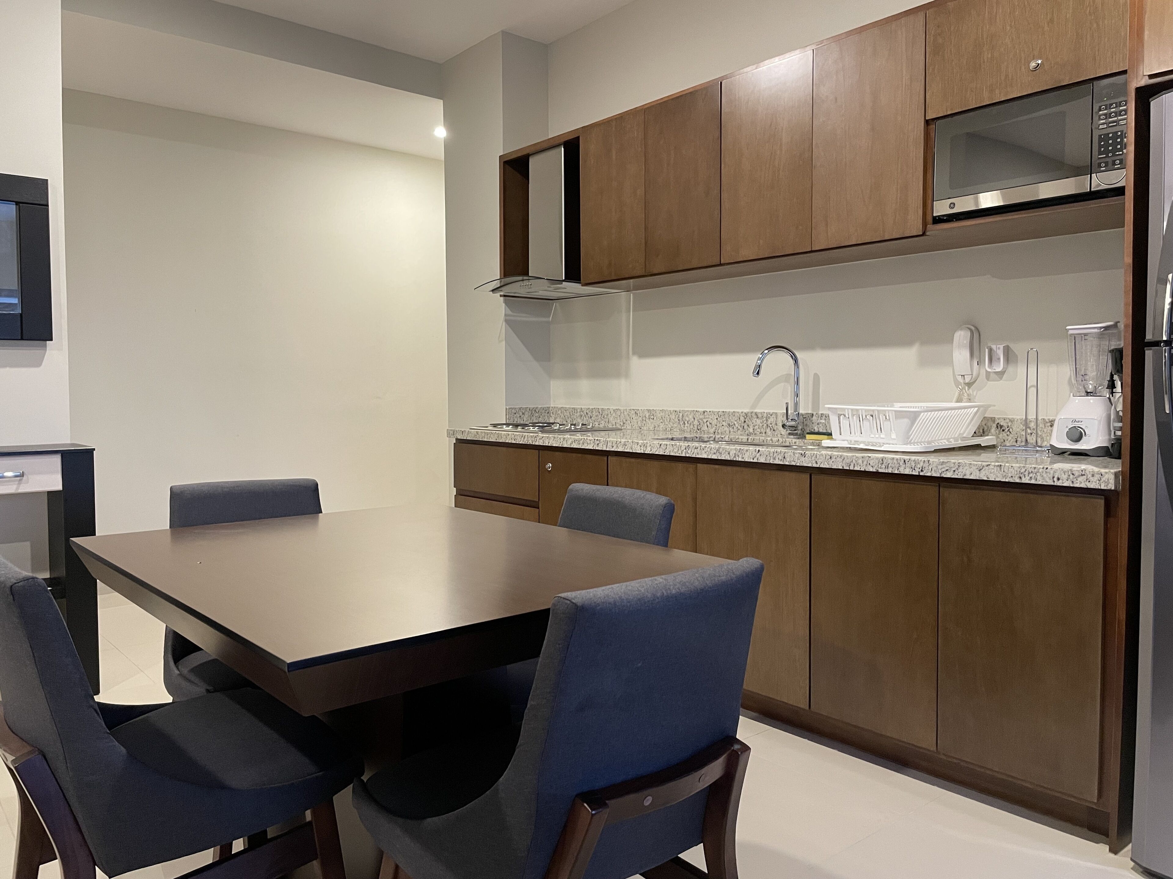 A modern kitchen with wooden cabinets, a granite countertop, a built-in microwave, a sink, and a dining table with chairs.