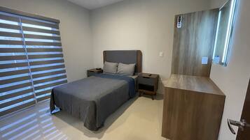 Un dormitorio con cama, mesitas de noche, un armario de madera y una ventana con persianas.