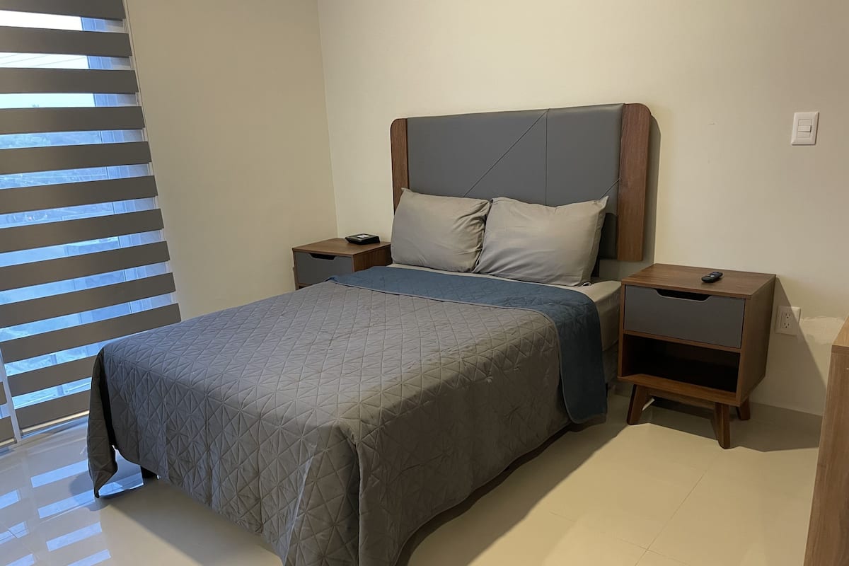 Un lit bien fait, recouvert d’une courtepointe, deux tables de chevet et une petite table de nuit avec une lampe.