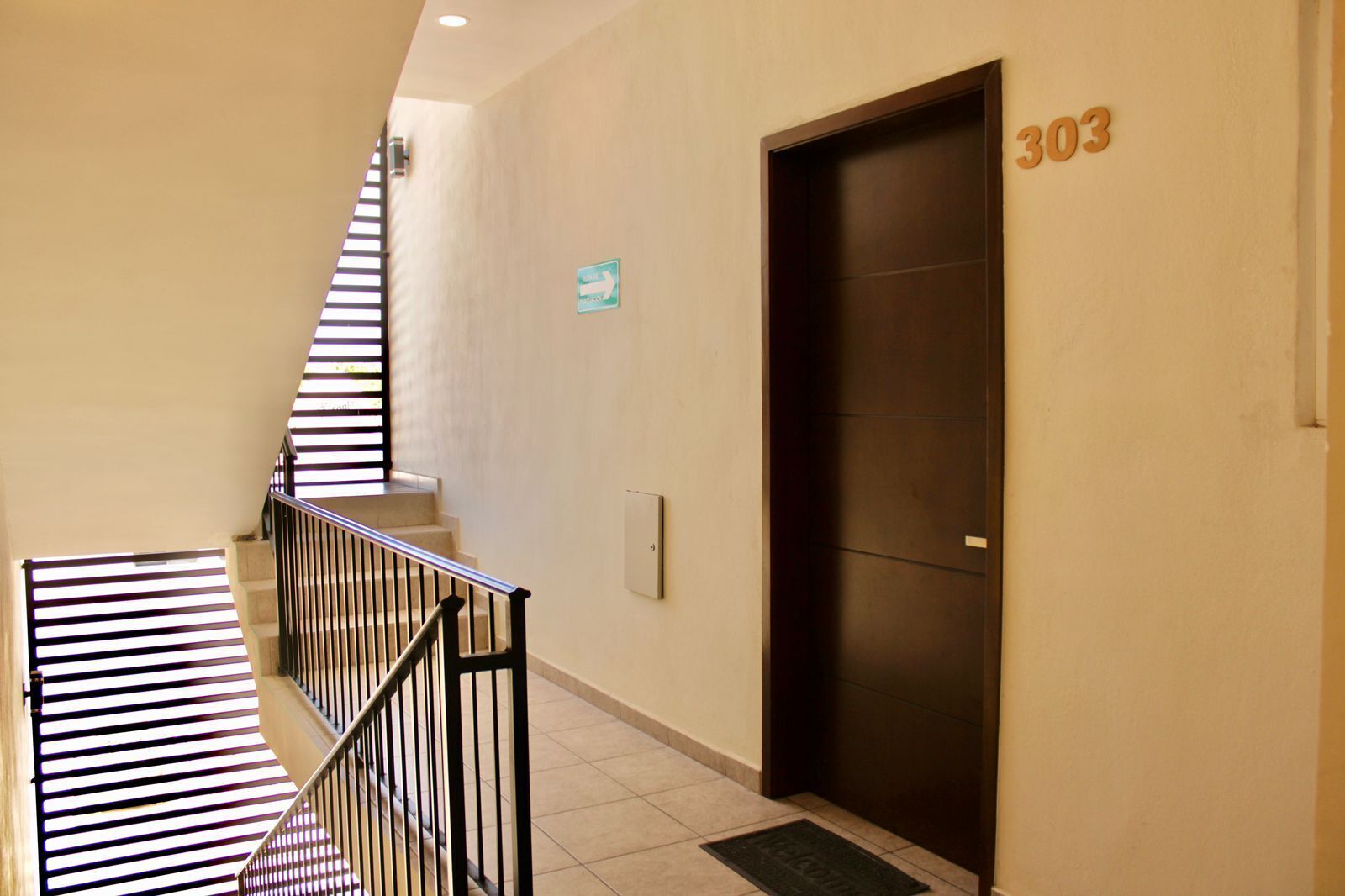 A hallway with a staircase, a door marked with the number 303, and a directional sign.