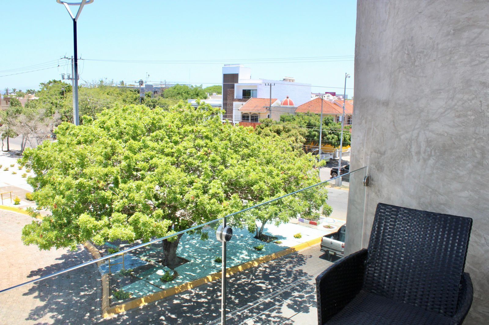 Un balcon donnant sur un arbre, avec une chaise et un bâtiment en arrière-plan.
