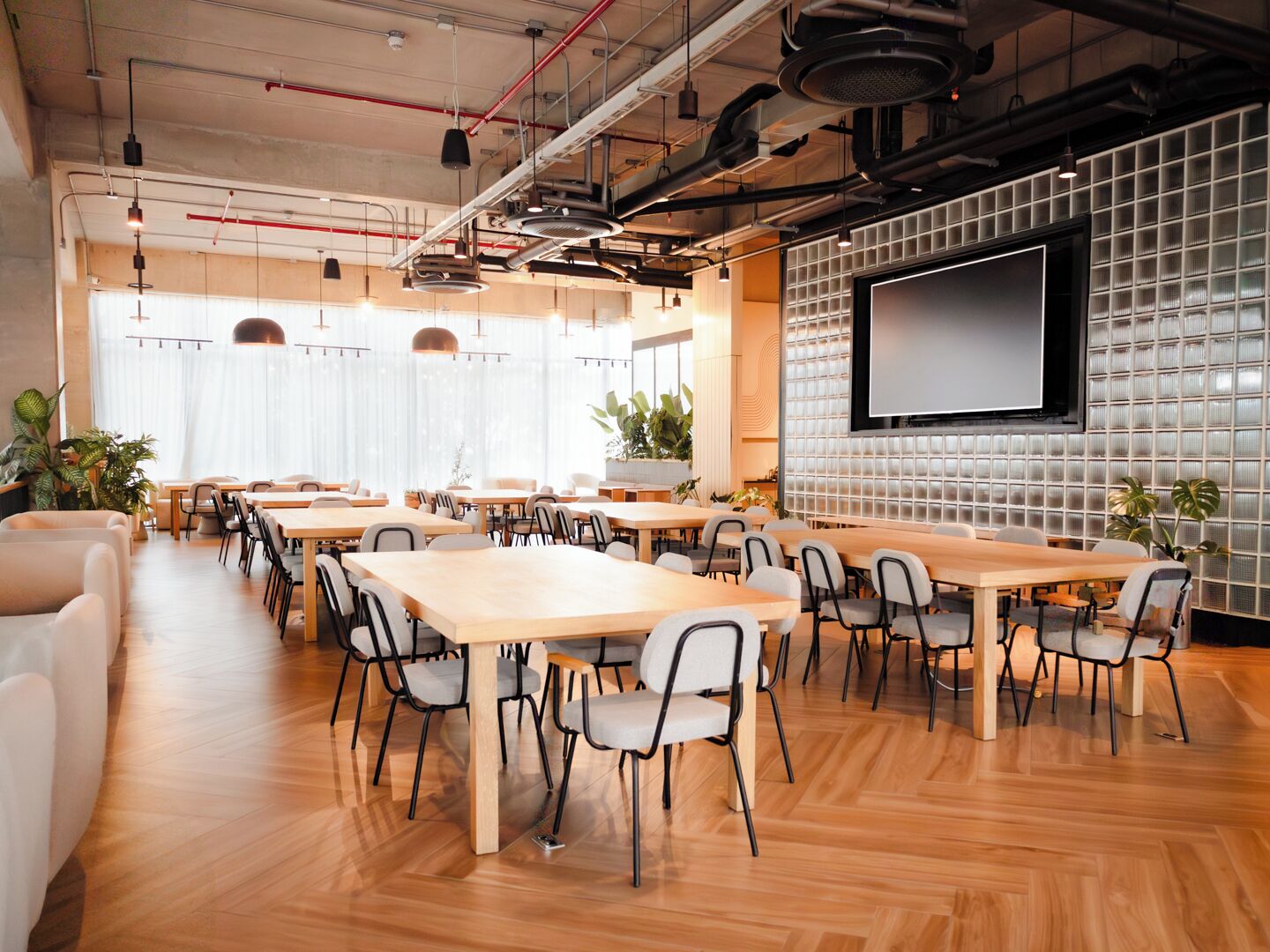 Una sala de conferències amb diverses taules i cadires, una pantalla gran i un sostre d'estil industrial modern.