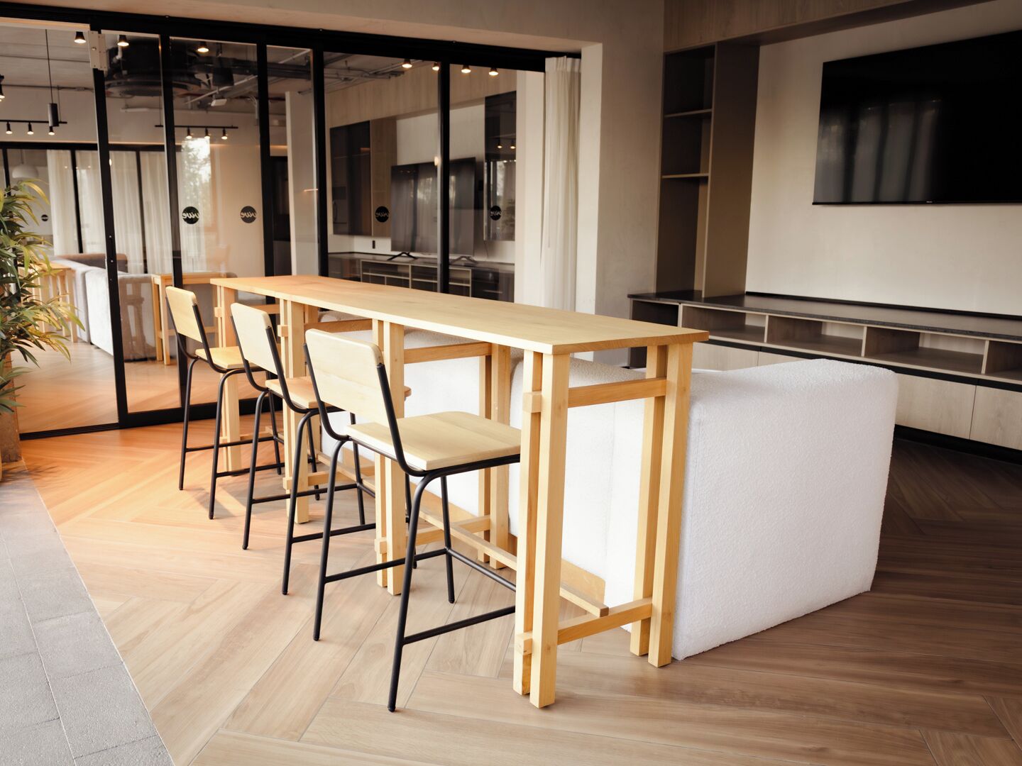 A modern office space with a long wooden table, four chairs, and a white cushioned bench.