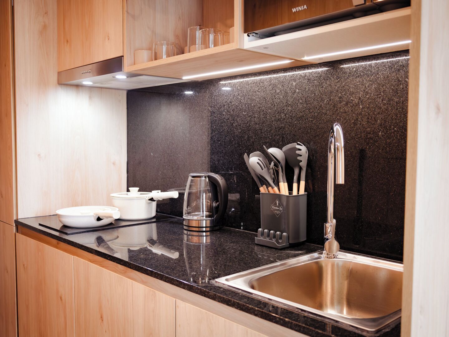 A modern kitchen with wooden cabinets, a granite countertop, stainless steel sink, and various kitchen appliances.