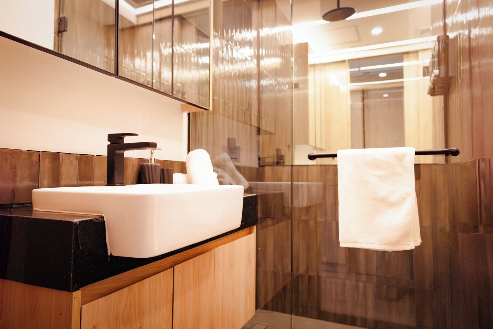 Un baño moderno con un lavamanos blanco, muebles de madera, cabina de ducha de vidrio y un perchero para toallas.