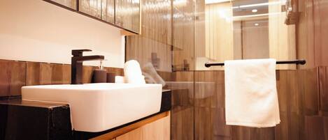 Un baño moderno con un lavamanos blanco, muebles de madera, cabina de ducha de vidrio y un perchero para toallas.