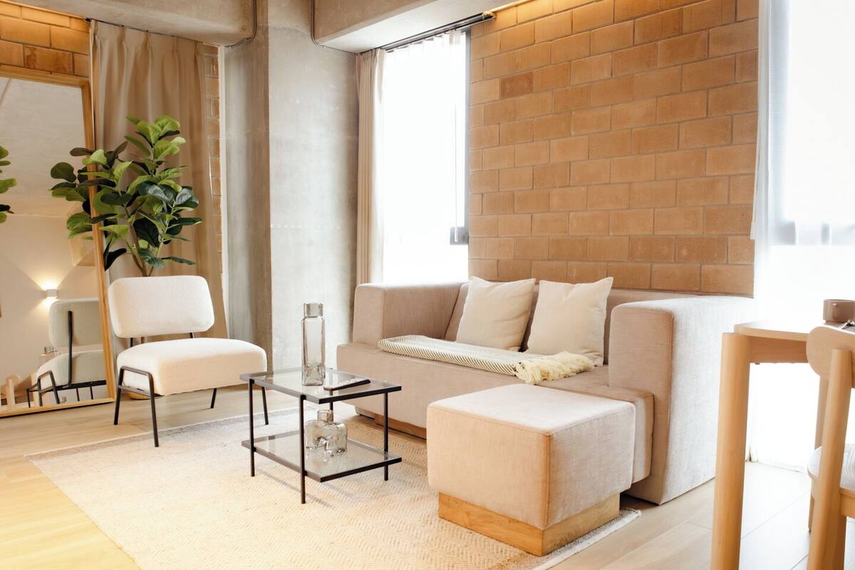 Una sala de estar moderna con un sofá, dos sillones, una mesita de centro y una pared de ladrillo.