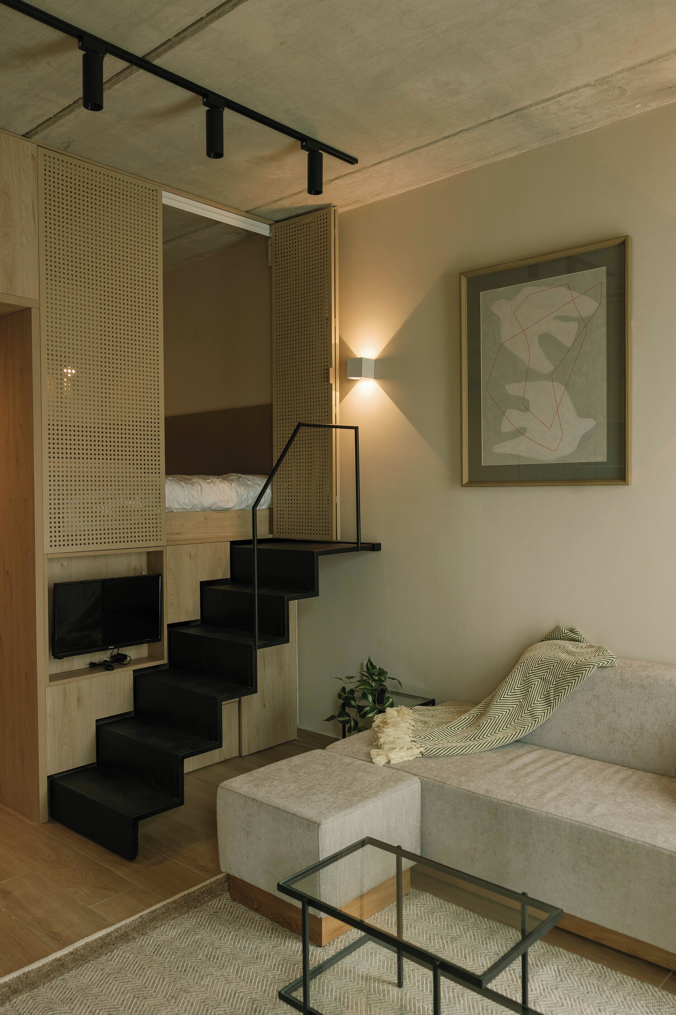 Una sala de estar moderna con un sofá, una mesa de centro de vidrio, un televisor, una escalera y un cuadro abstracto enmarcado.