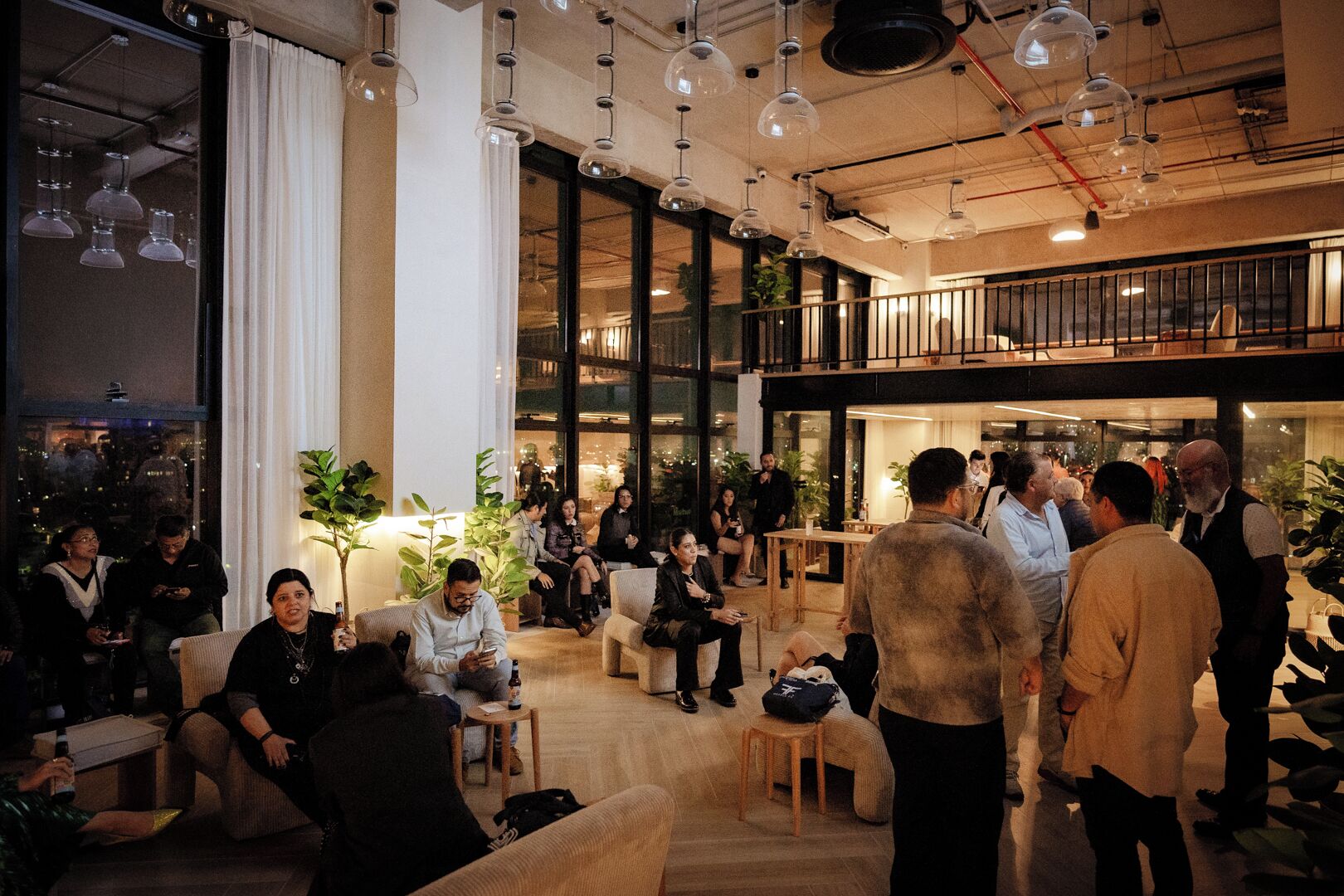 Un vaste espace intérieur doté de plusieurs coins salon, de grandes fenêtres et de luminaires suspendus.