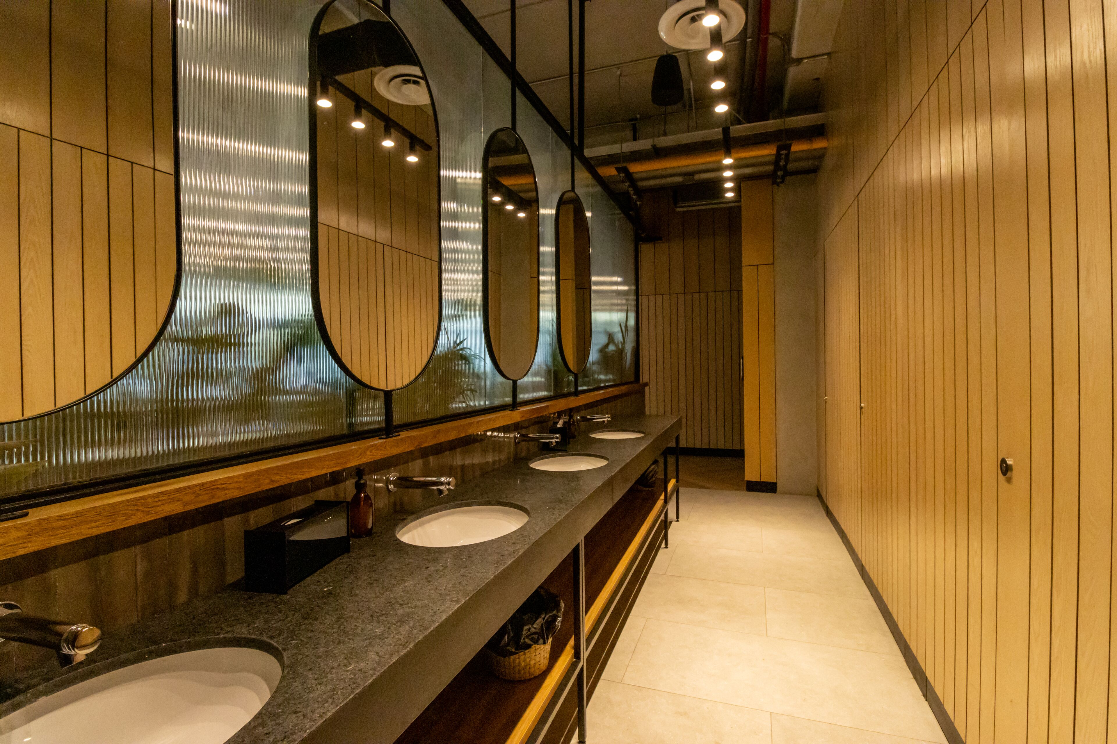 A modern bathroom with three sinks, large mirrors, and wooden paneling.
