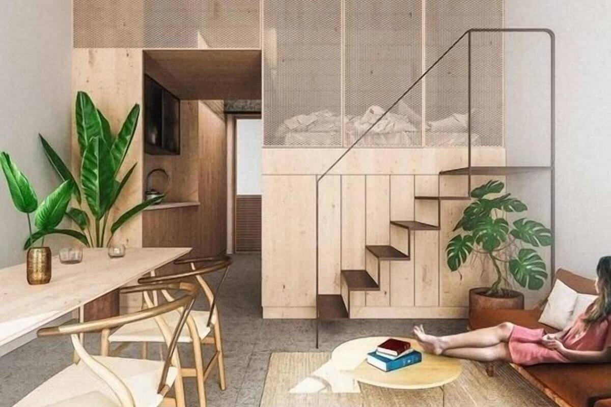 Un interior moderno con zona de comedor, escalera y un área de estar con una persona leyendo.