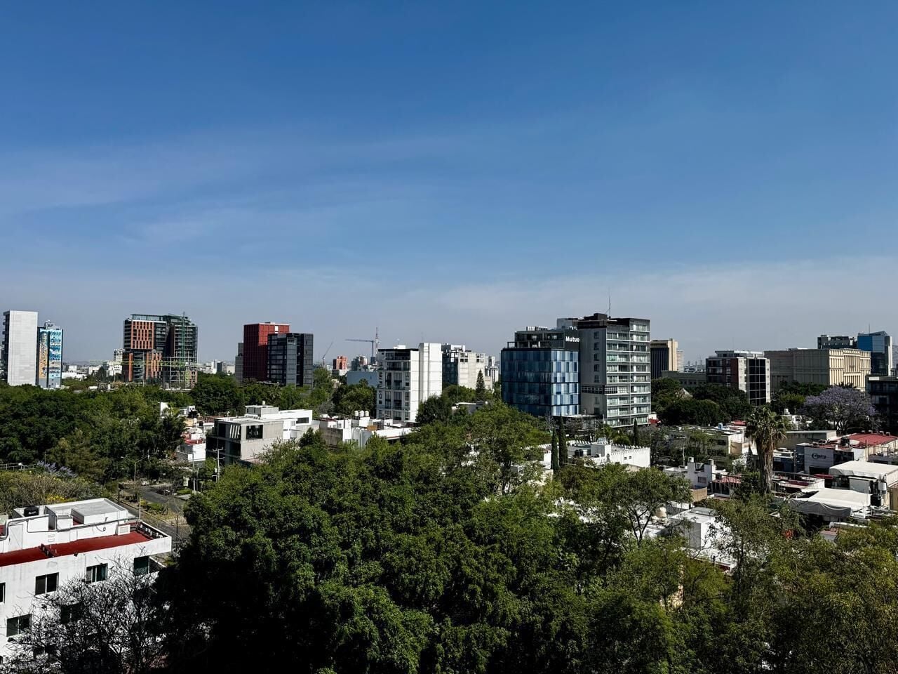 A cityscape with modern buildings, dense greenery, and a clear sky.