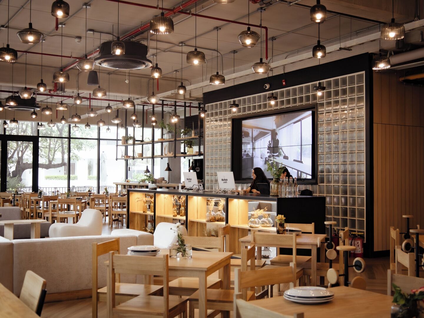 Un café moderno con mobiliario de madera, iluminación colgante, una pantalla de televisión grande y vistas al exterior.