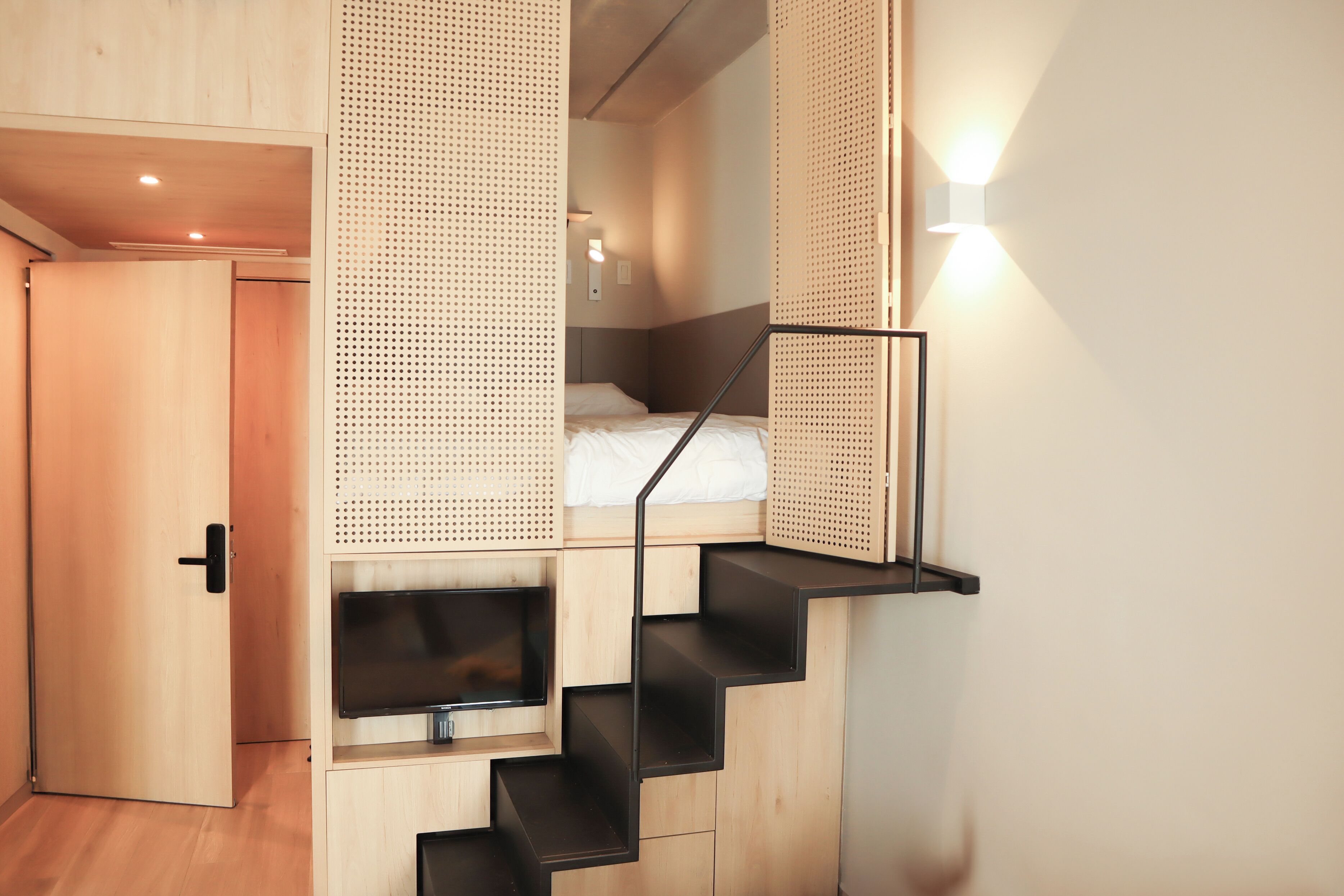 Une petite pièce comprenant un lit, un téléviseur et un escalier.
