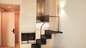 Una habitación pequeña con cama, televisión y una escalera.