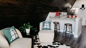 A modern kitchen with dark wooden walls, a white island with stools, and a cowhide rug. - Stunning, Secluded A-Frame w/ Hammock and Tree Top View (New Braunfels)