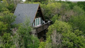 A cabin with a sloped roof, a balcony, surrounded by dense greenery. - Stunning, Secluded A-Frame w/ Hammock and Tree Top View (New Braunfels)