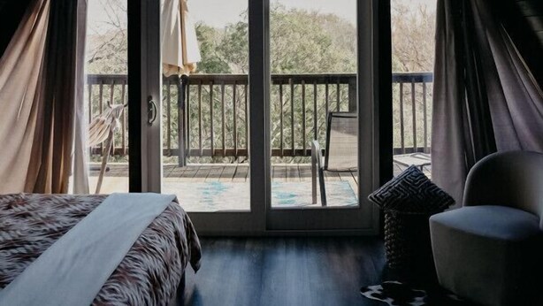 A bedroom with a bed, a chair, a ceiling fan, and a view of the outside balcony. - Stunning, Secluded A-Frame w/ Hammock and Tree Top View (New Braunfels)