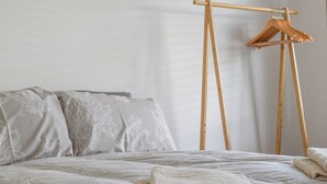 Un lit bien fait, recouvert d’une couvre-lit à motifs, un porte-manteau en bois et une pile de serviettes pliées.