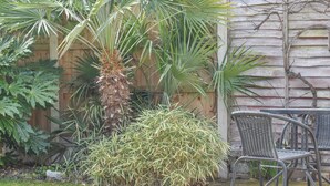 Un espace extérieur aménagé avec une chaise en métal, un palmier et diverses plantes.