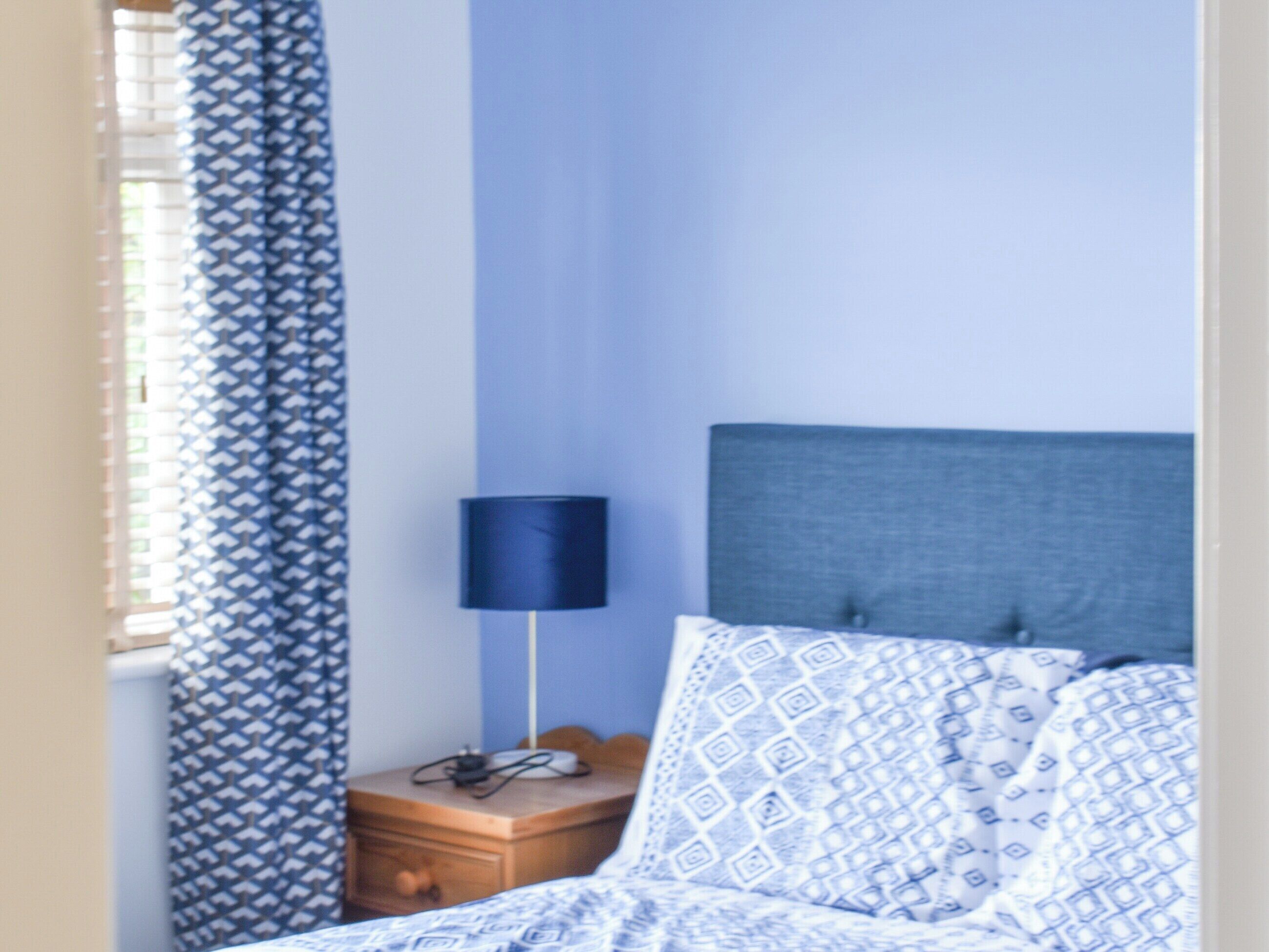 A bedroom with a bed, a bedside table, a lamp, and a patterned curtain.