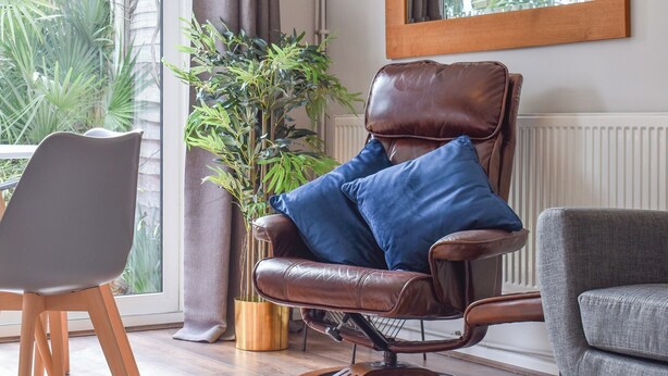 Un fauteuil en cuir avec des coussins bleus, placé près d’une fenêtre donnant sur un paysage verdoyant.