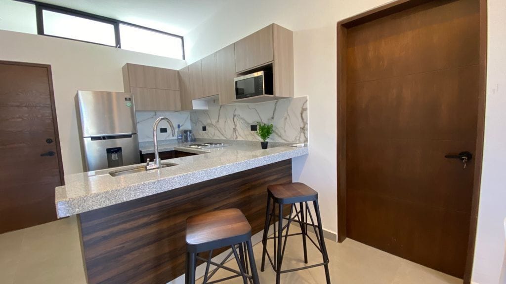 Una cocina moderna con encimera de mármol, electrodomésticos de acero inoxidable y taburetes de bar de madera.