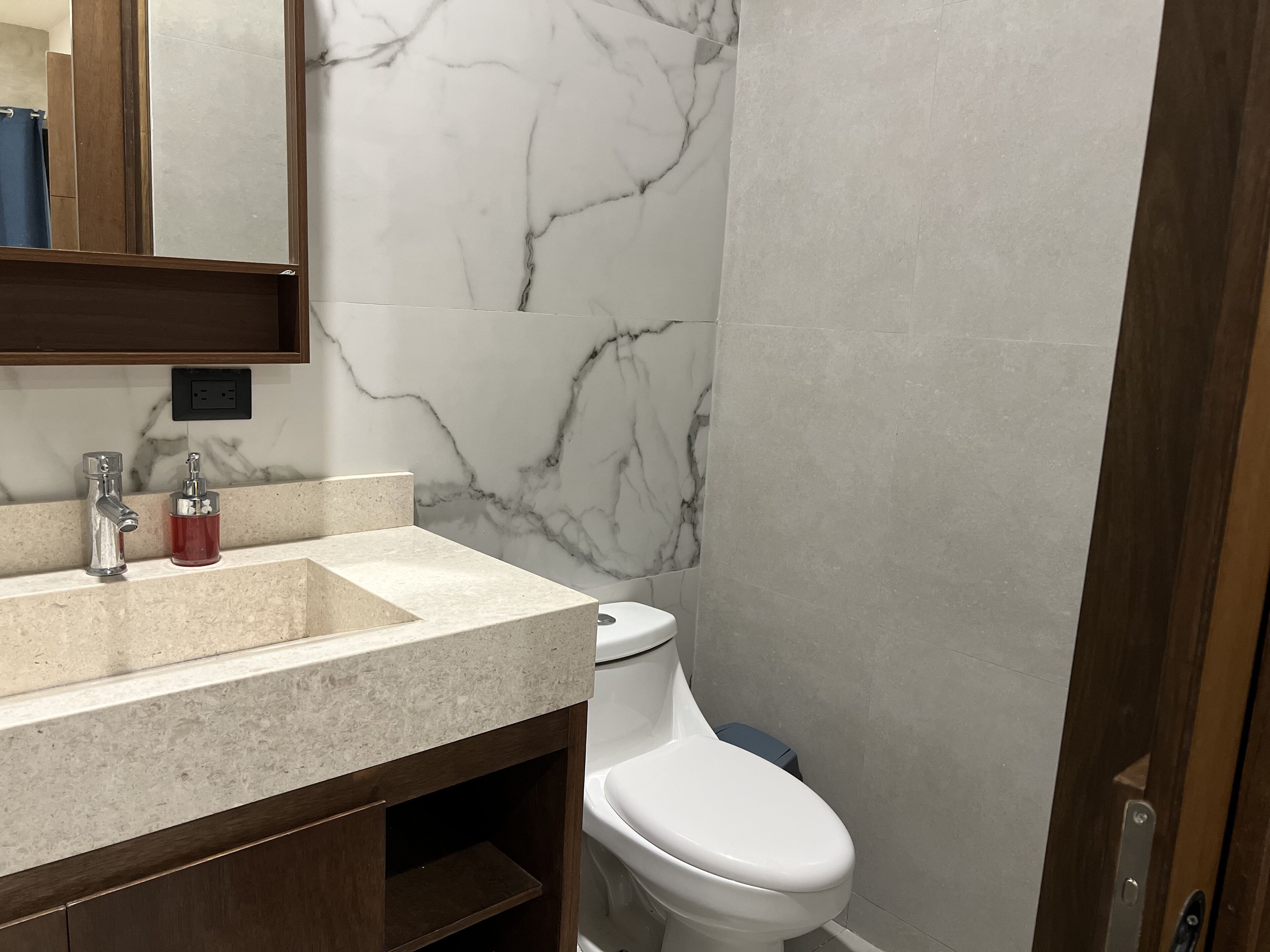 A bathroom with a marble wall, a sink with a faucet, a soap dispenser, and a toilet.