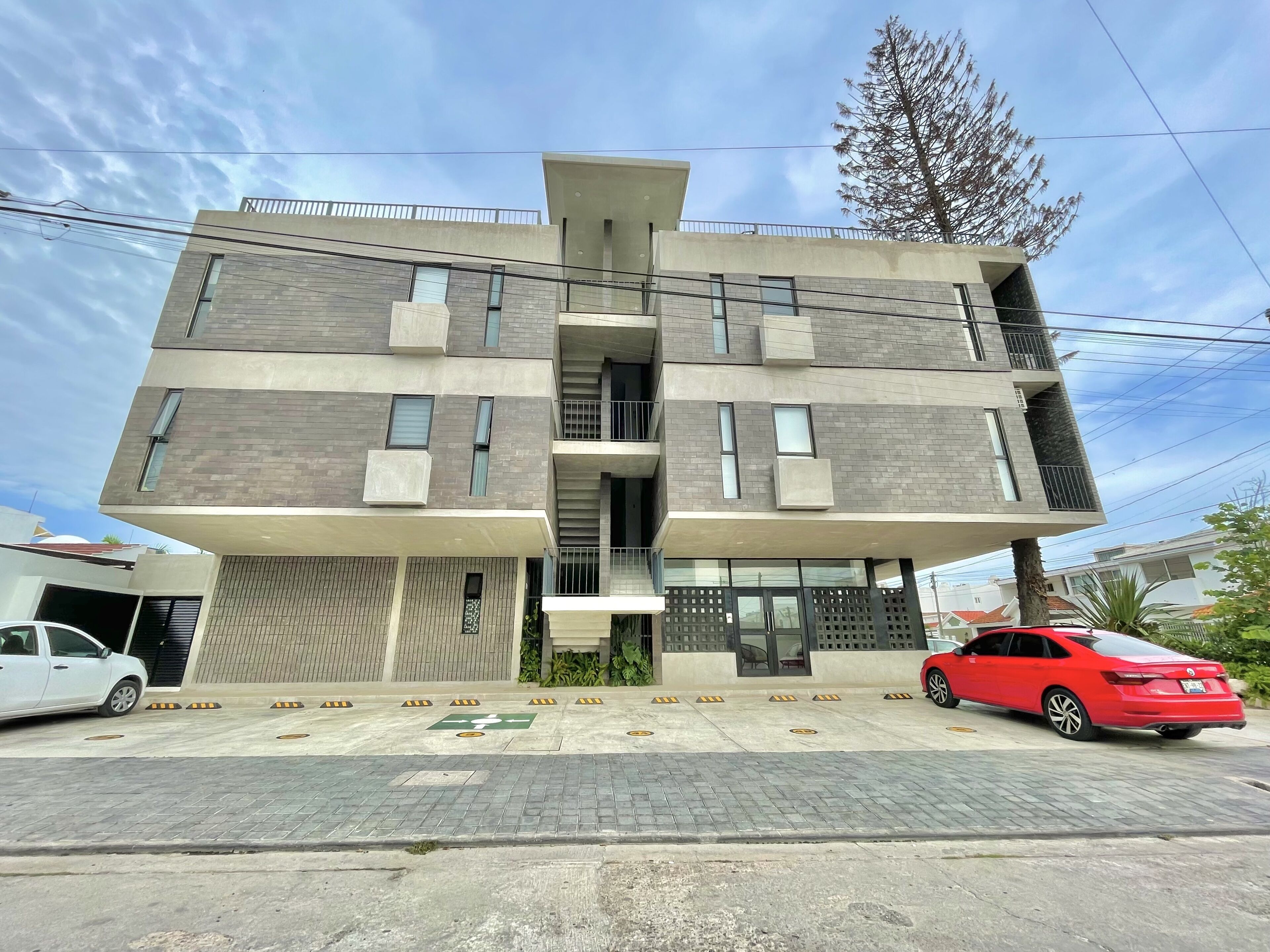 A modern multi-story building with a flat roof, large windows, and balconies.
