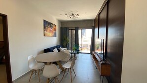 Un salon moderne avec une table à manger ronde, des chaises blanches, un canapé bleu et une grande fenêtre avec des rideaux.